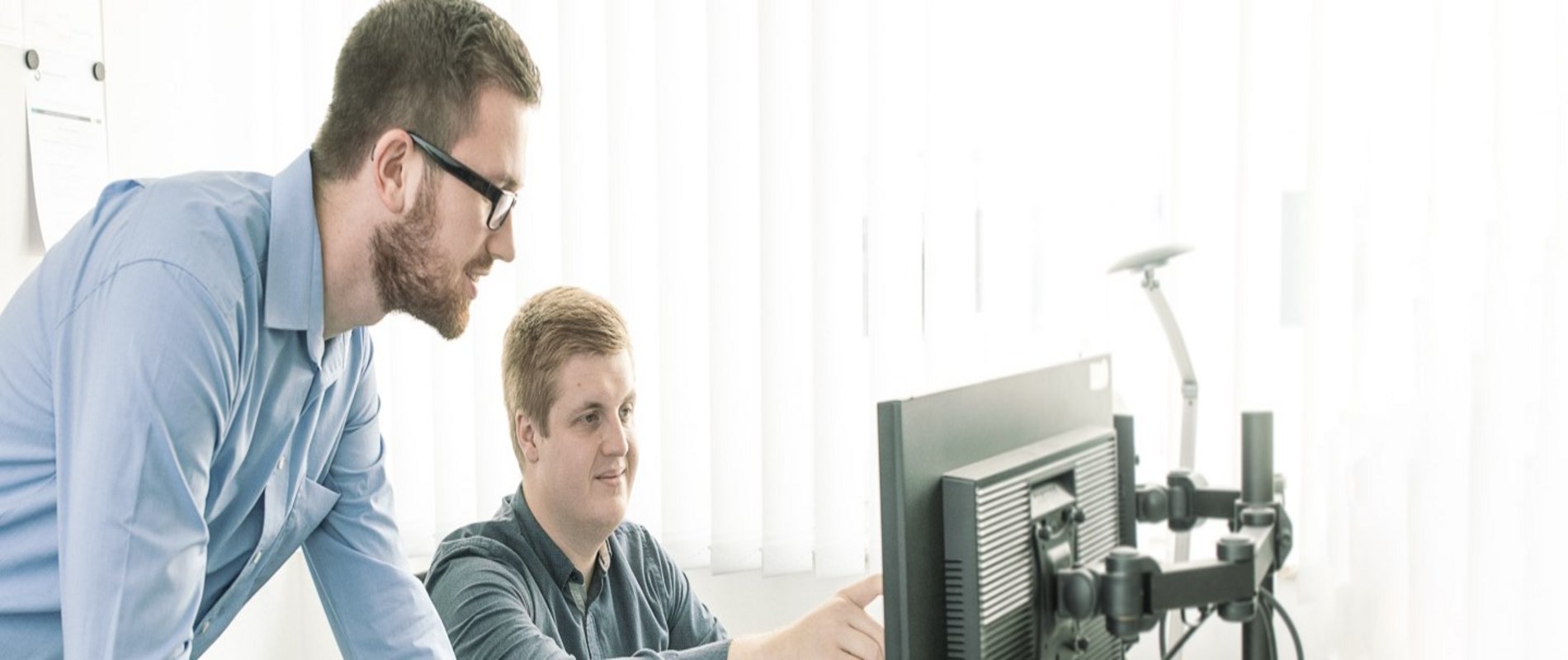 Zwei duale Studenten schauen gemeinsam auf einen Monitor