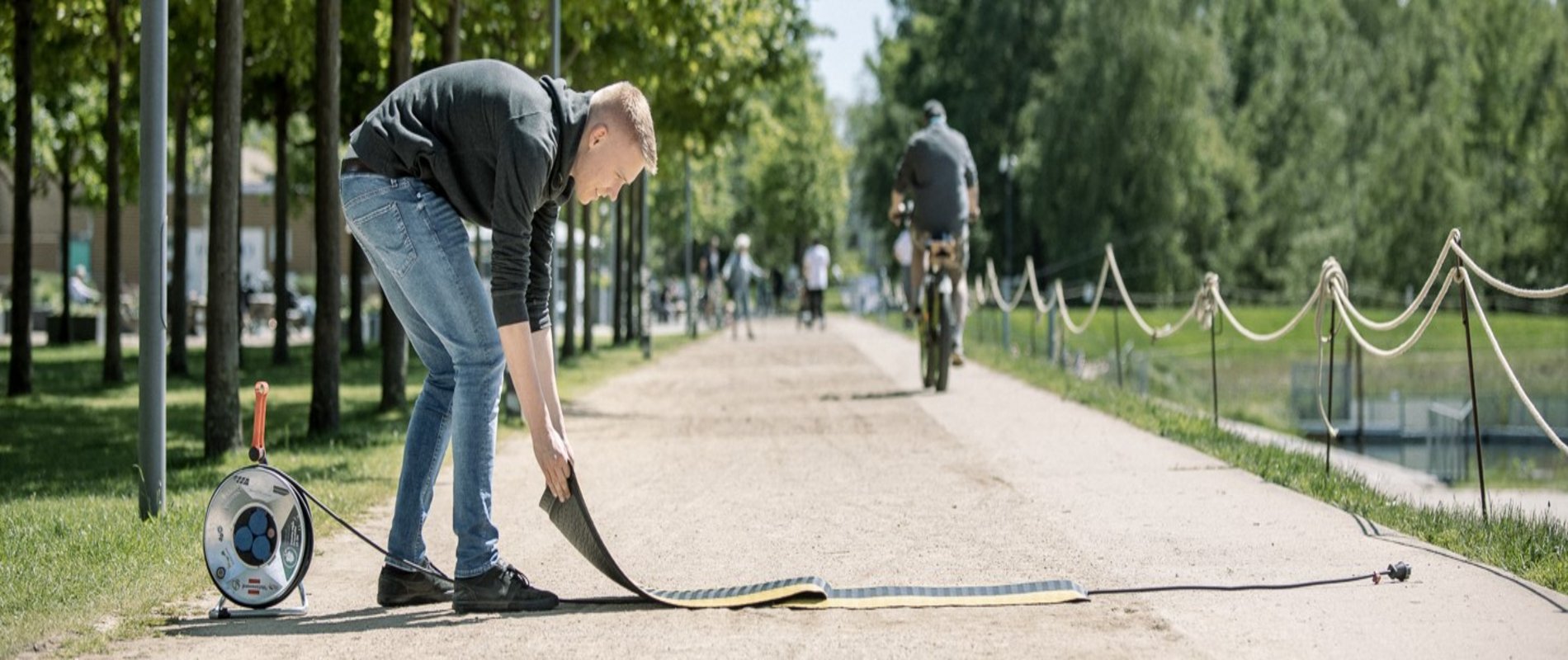 Ein Auszubildener baut im Stadtpark für eine Veranstaltung auf und bedeckt ein Stromkabel mit einer Schutzmatte